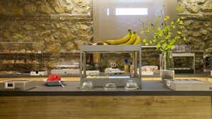 A breakfast bar with a stone wall backdrop, a fruit display, and a coffee station. - Hotel Plana (Caserta)
