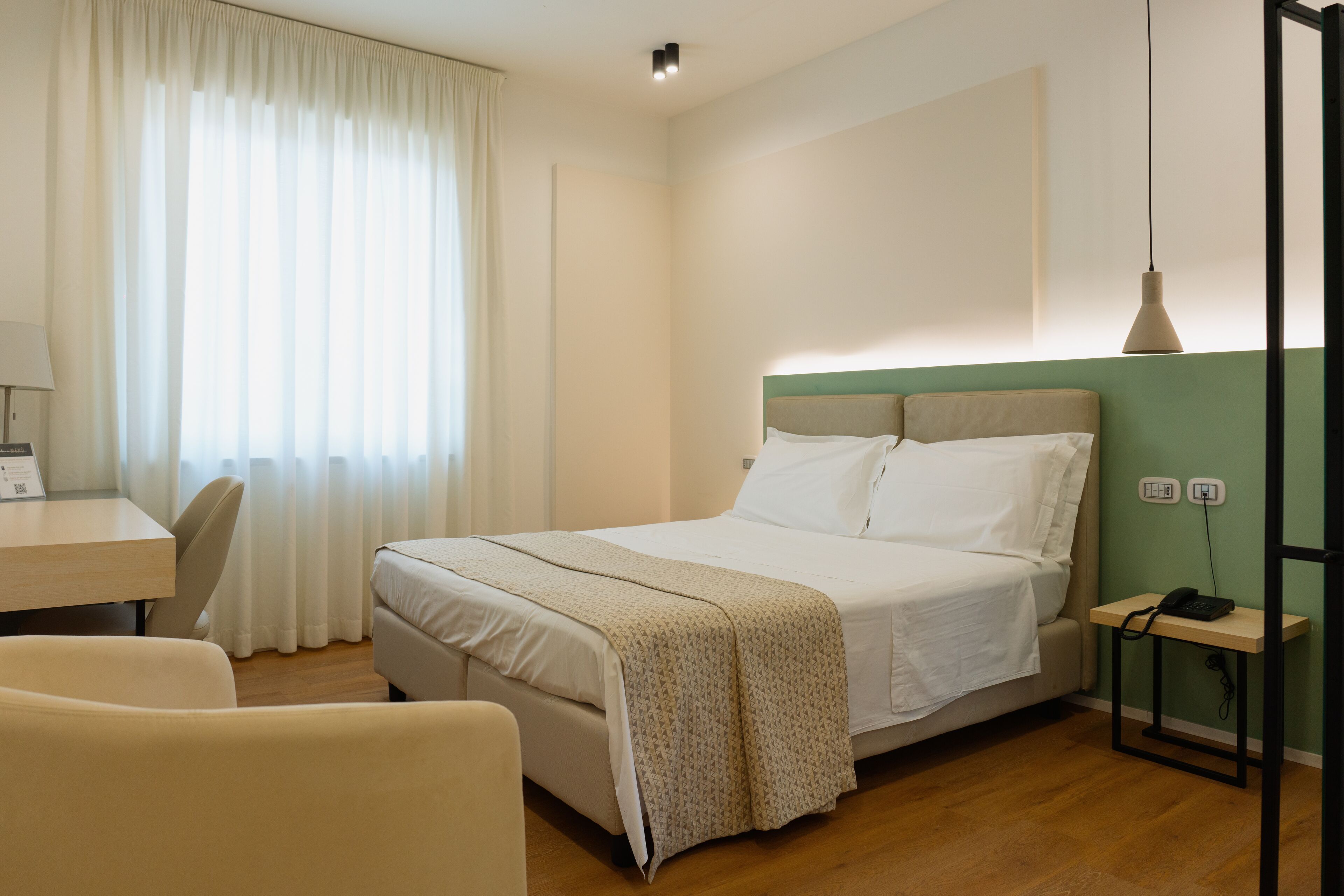 A hotel room with a bed, a desk, a chair, and a bedside table with a phone.