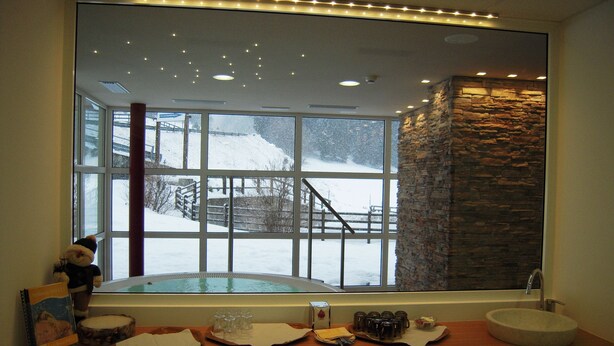 A bathroom with a large window, a stone accent wall, and a wooden vanity with a sink and various toiletries. - Seggiovia (Folgaria)