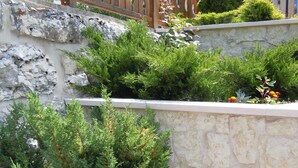 A stone retaining wall with various shrubs and flowers, a wooden fence, and a building in the background. - Seggiovia (Folgaria)