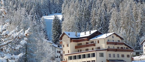 A multi-story hotel with a snow-covered landscape and forest in the background.