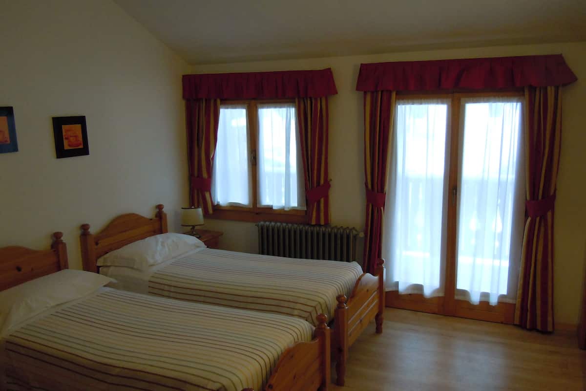 A room with two wooden beds, a radiator, and curtains on the windows.