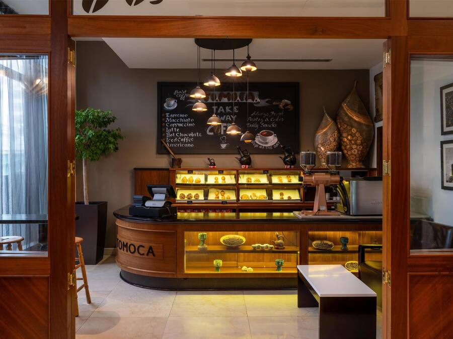 Interior de uma cafeteria, com um balcão exibindo diversas opções de café e um quadro de cardápio acima.