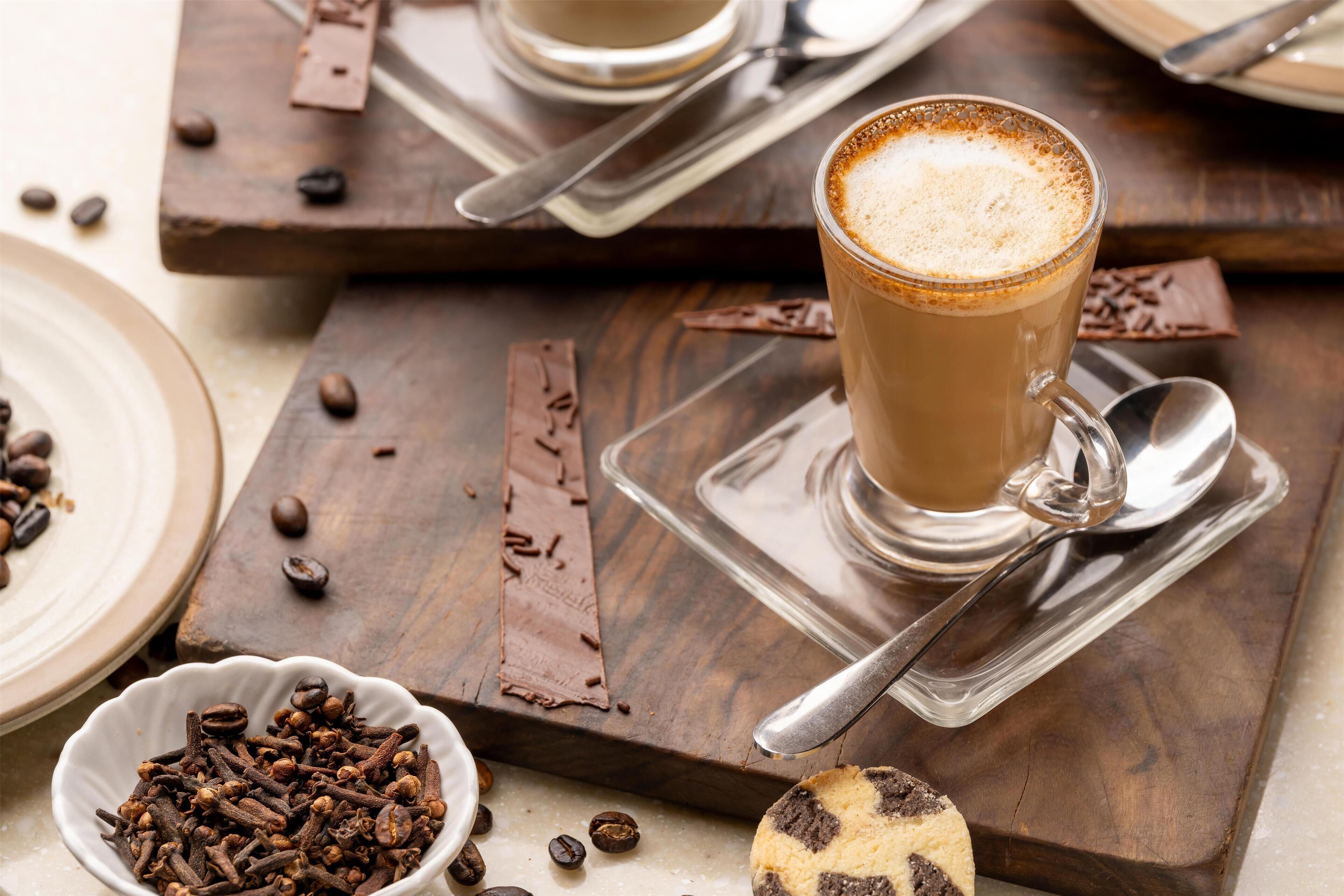 A cup of coffee on a wooden tray with a spoon and a cookie.