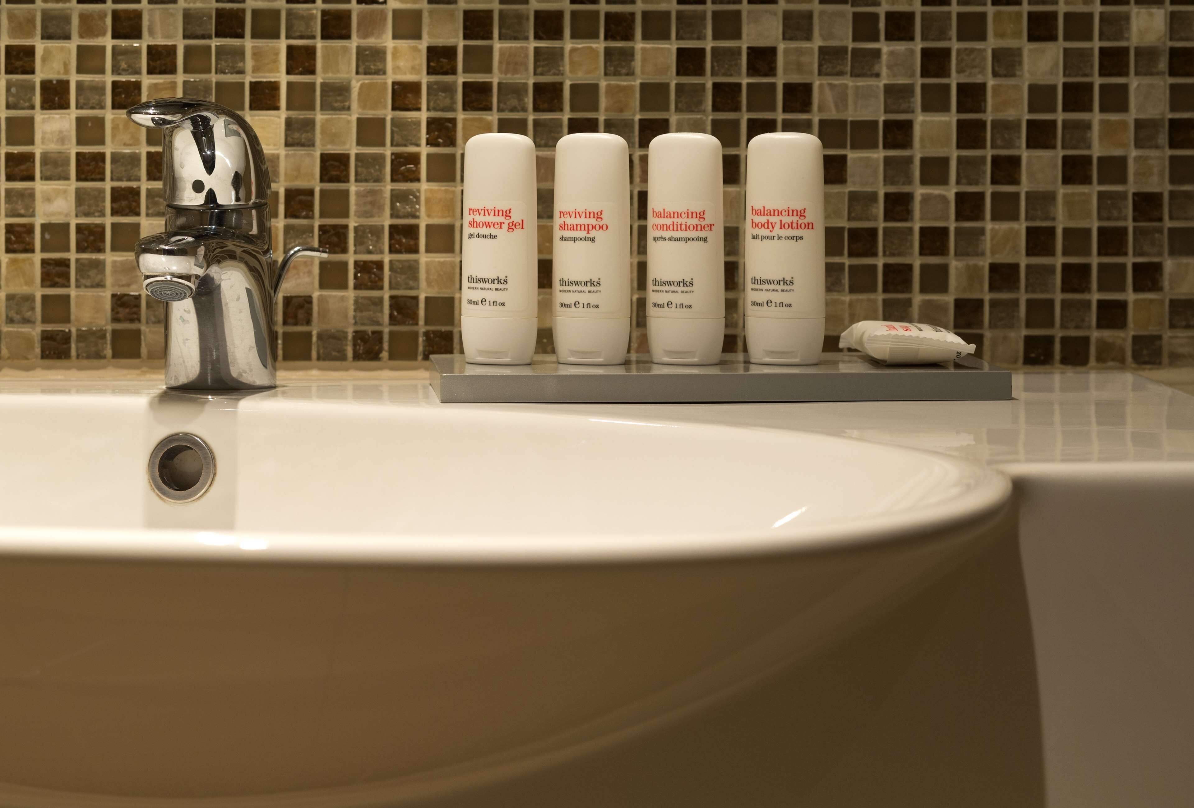 A bathroom sink with a chrome faucet and four bottles of toiletries on a tray.