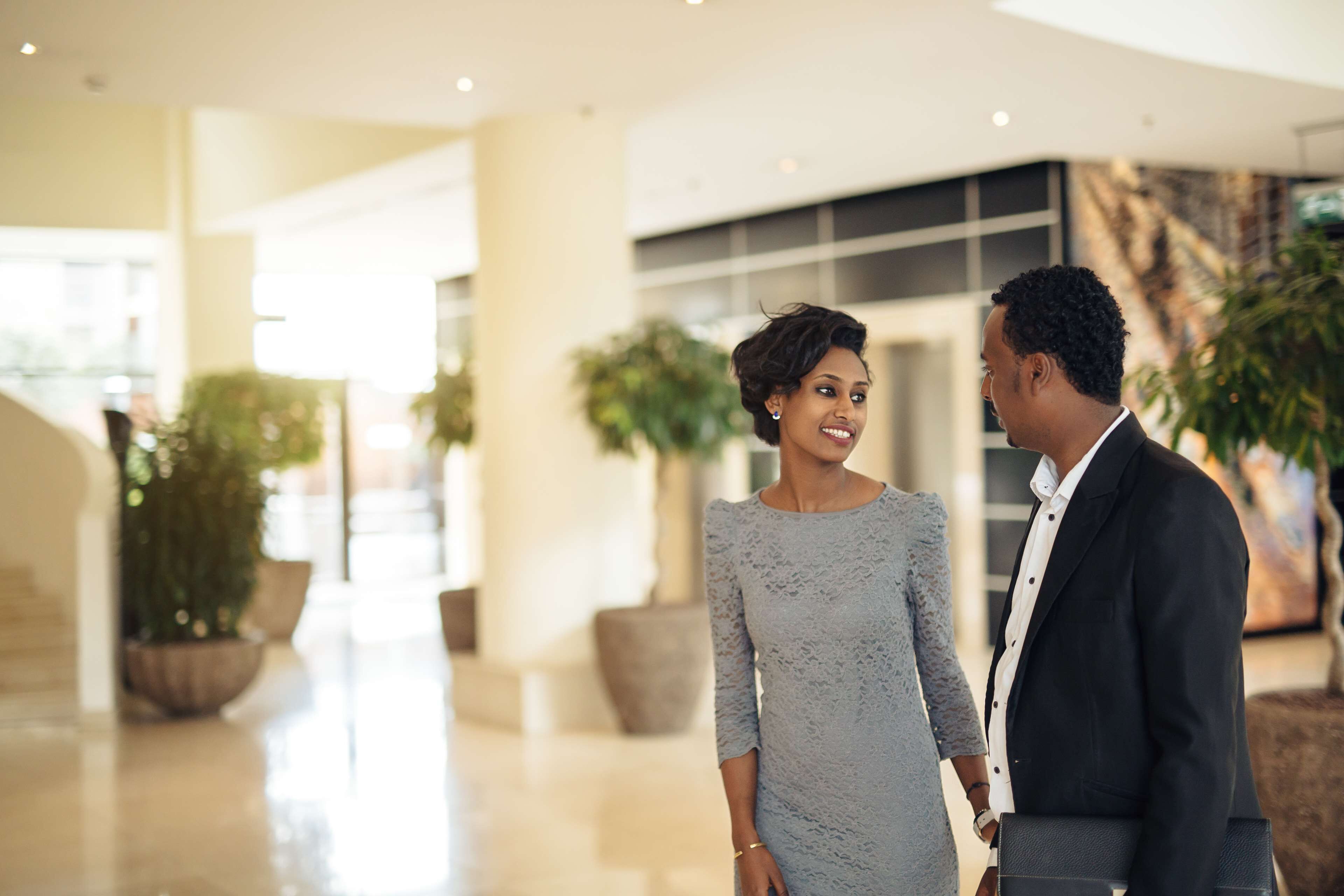 A couple holding hands in a modern indoor setting with potted plants and a polished floor.
