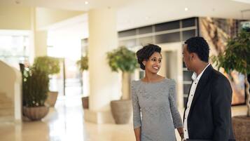 A couple holding hands in a modern indoor setting with potted plants and a polished floor.