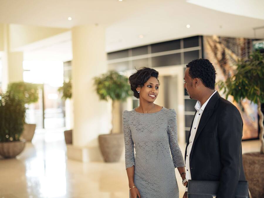 A couple holding hands in a modern indoor setting with potted plants and a polished floor.