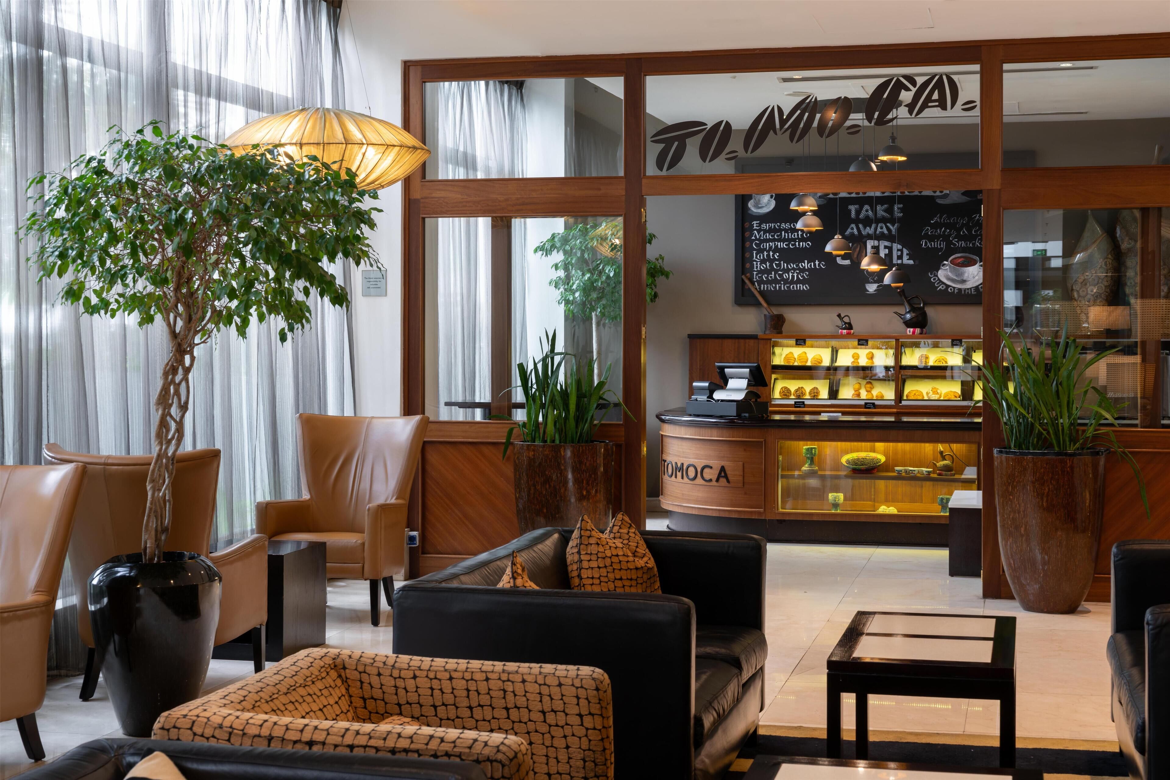 A modern hotel lobby with leather seating, a reception desk, and a coffee bar.