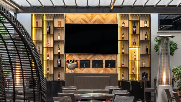 An outdoor seating area with wicker furniture, a large flat-screen TV, and a wall of illuminated shelves.