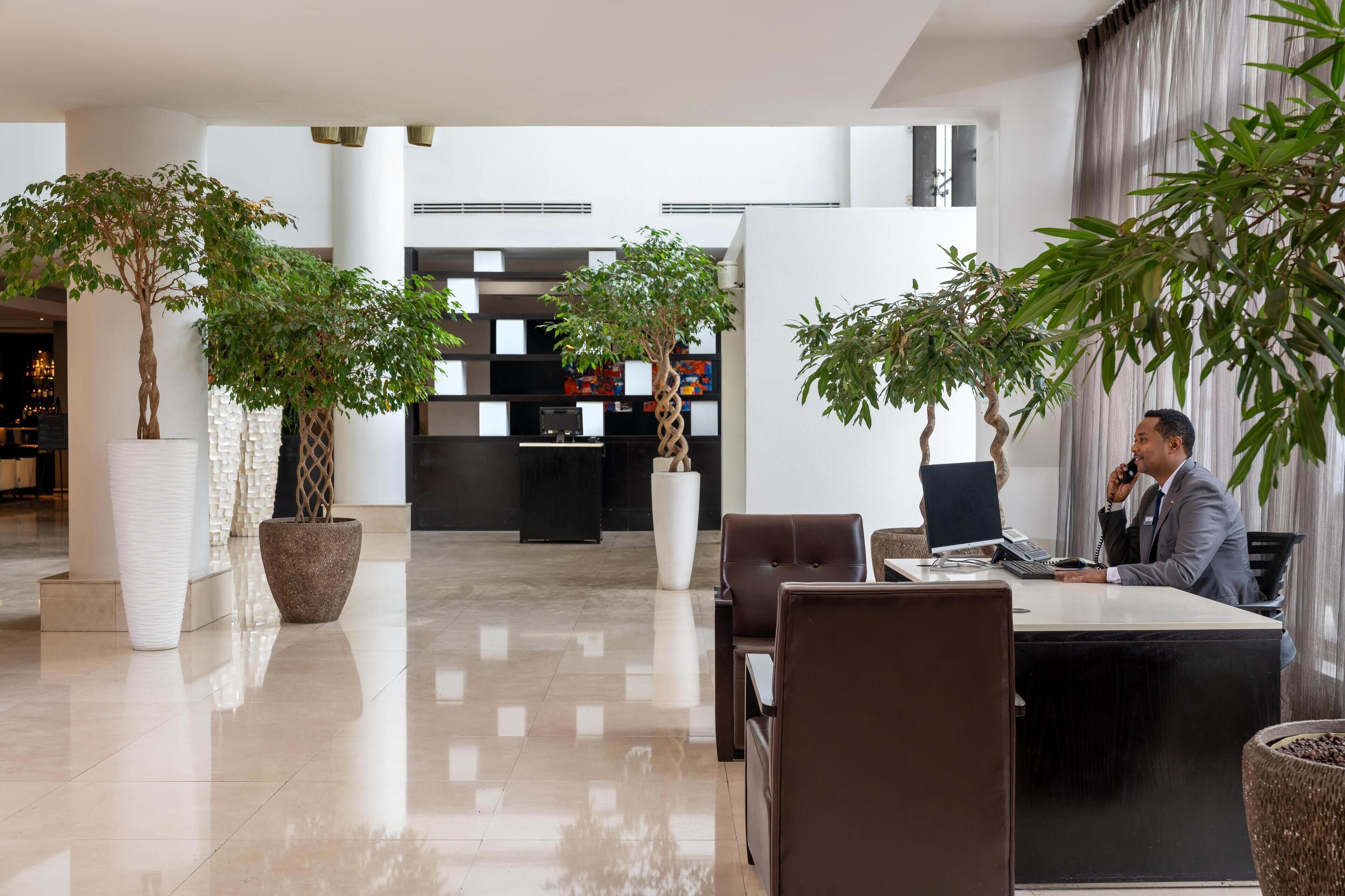 A modern lobby with a reception desk, seating area, and potted plants.
