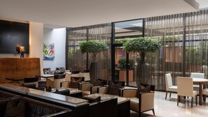 A modern lounge area with seating arrangements, large windows, and indoor plants.