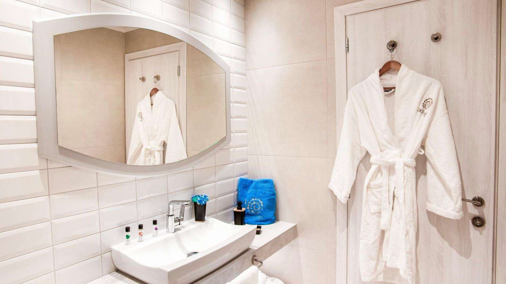 Un baño con un lavabo blanco, un espejo y una bata blanca colgada en la pared.