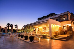 Un espacio al aire libre con mesas, sillas, un bar y una piscina al fondo.