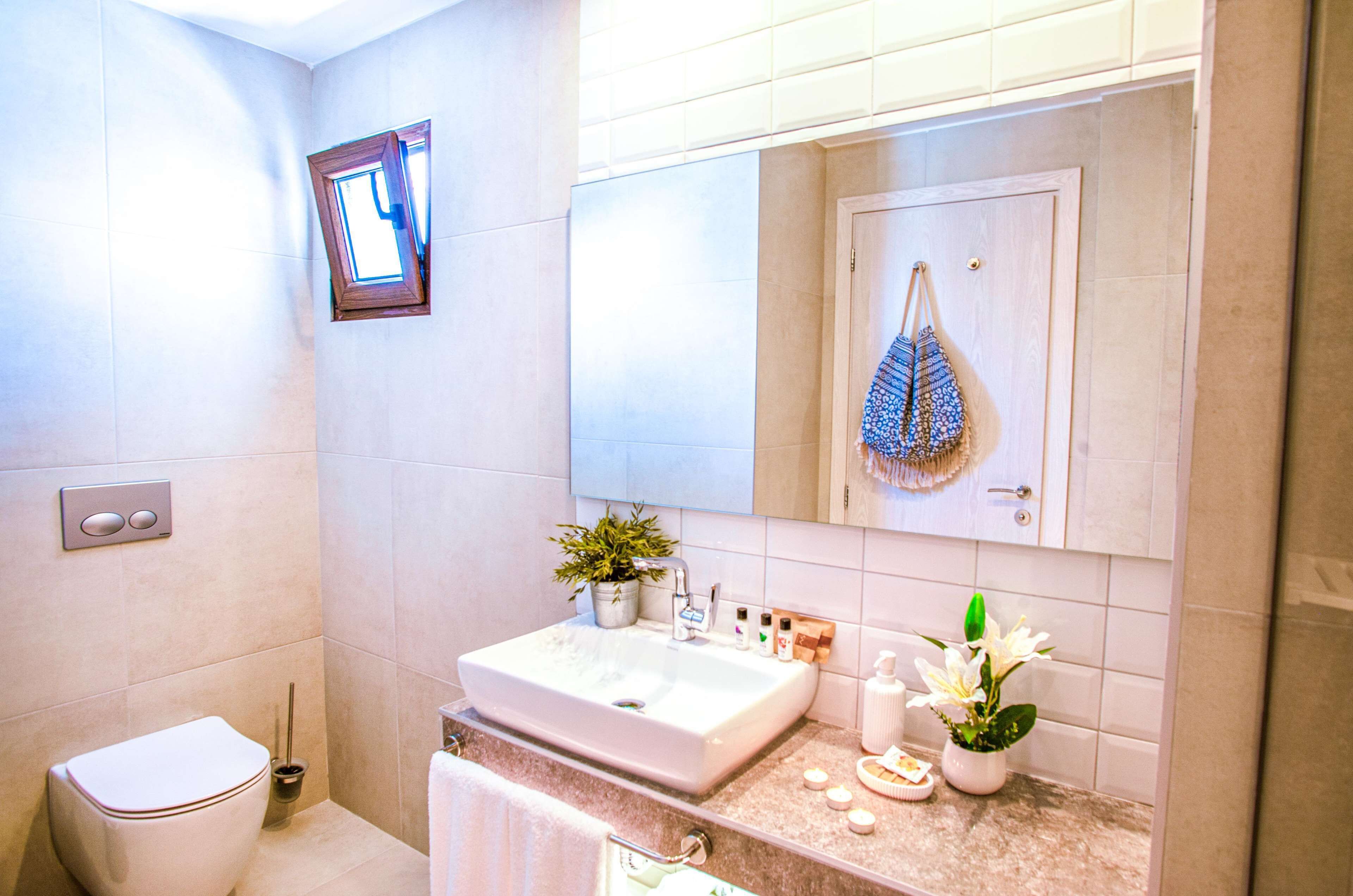 A bathroom with a toilet, sink, mirror, towel rack, and a small window.