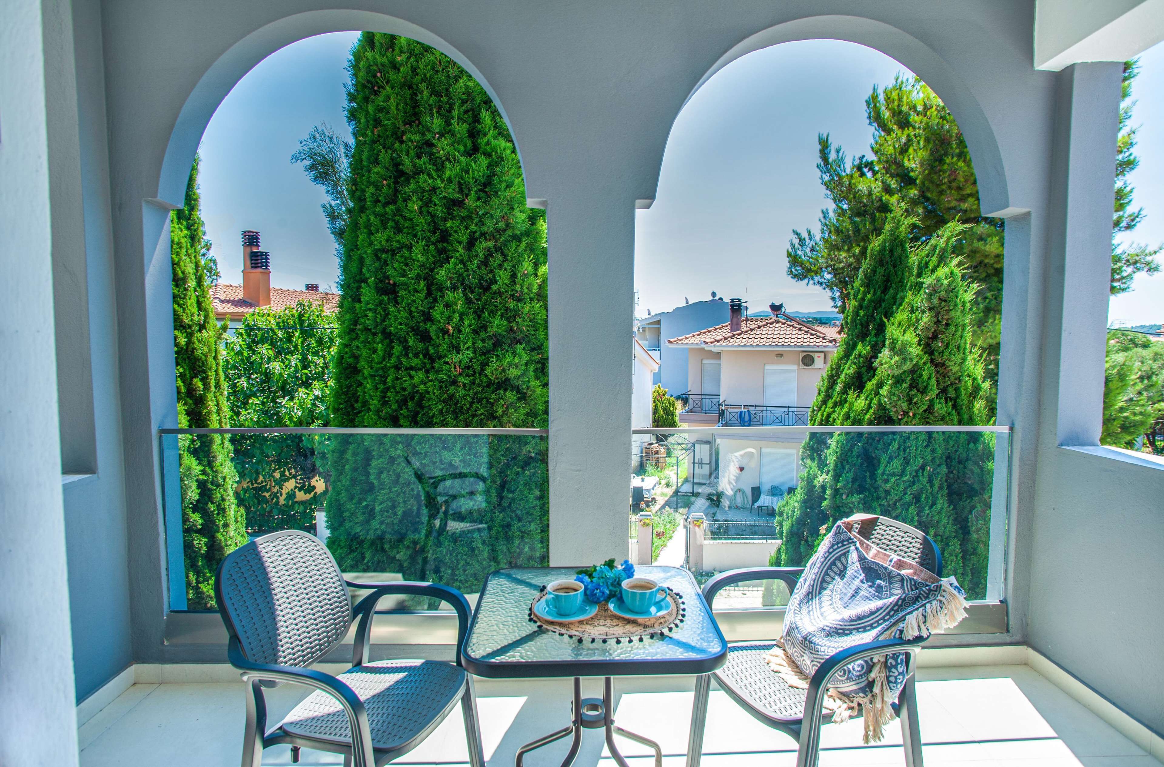 Ein Balkon mit zwei Stühlen, einem Tisch und Blick auf ein Gebäude mit Ziegeldach.