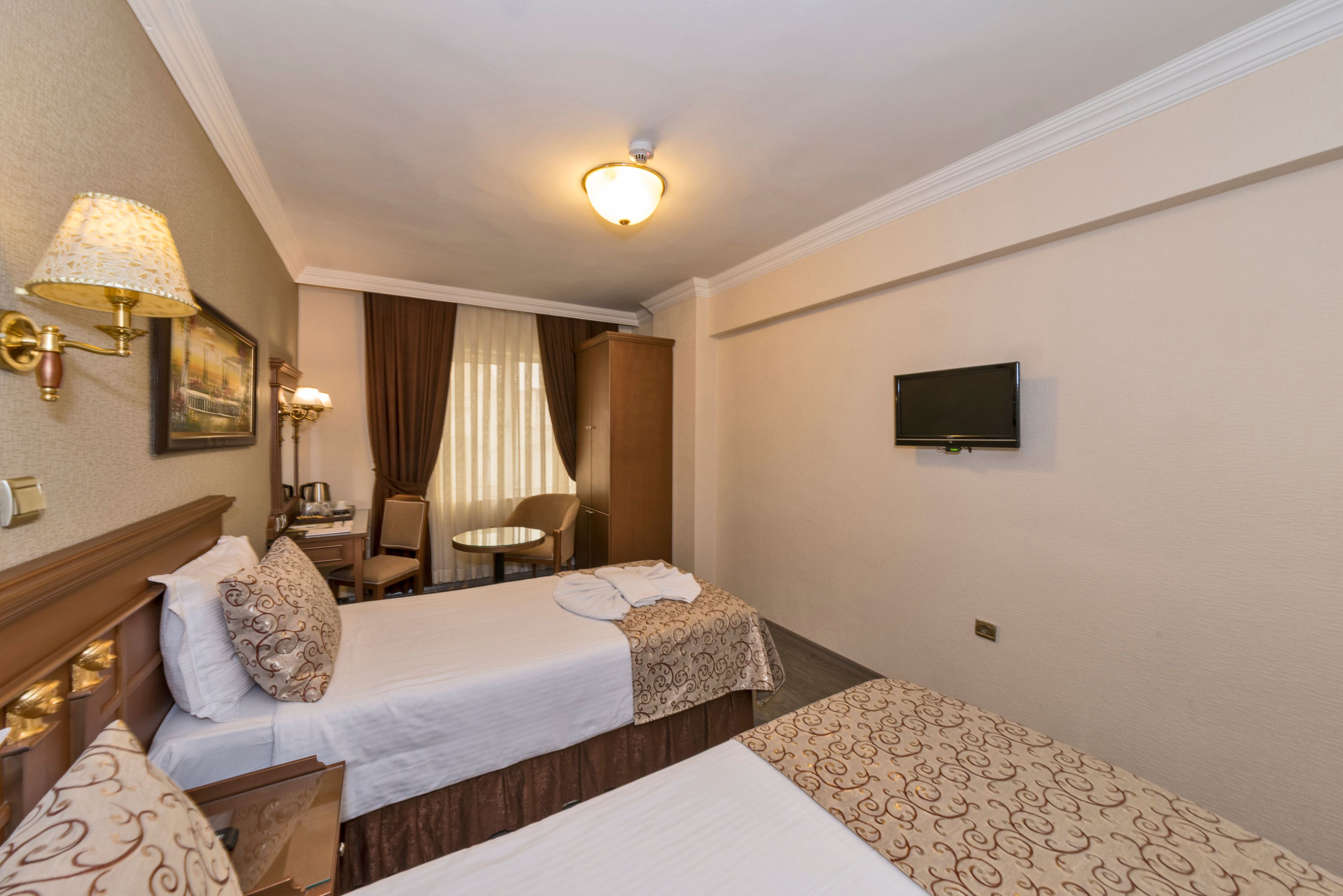 Een hotelkamer met twee bedden, een bureau, een stoel, een televisie en een plafondlamp.