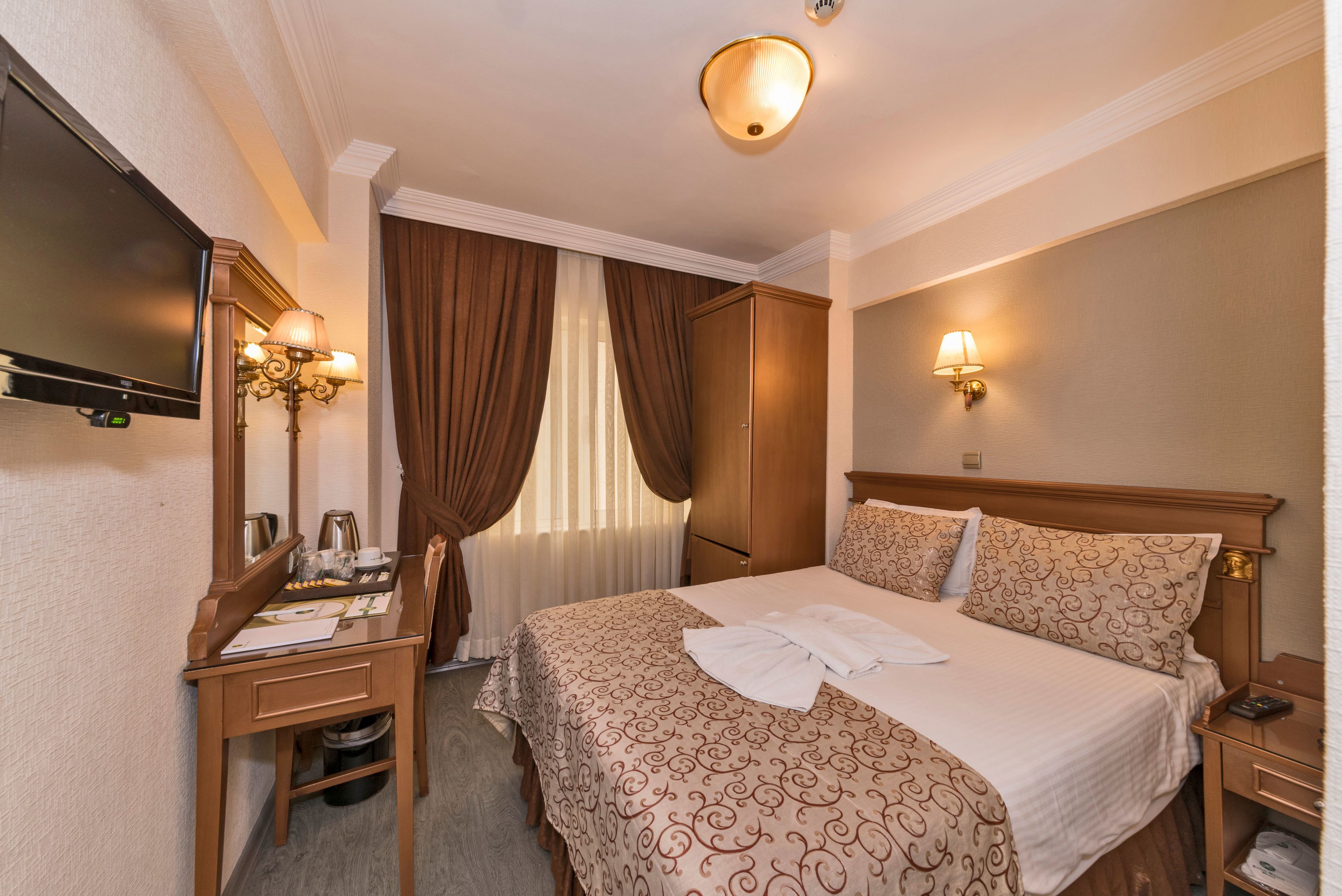 A hotel room with a bed, a desk, a chair, a television, and a wardrobe.