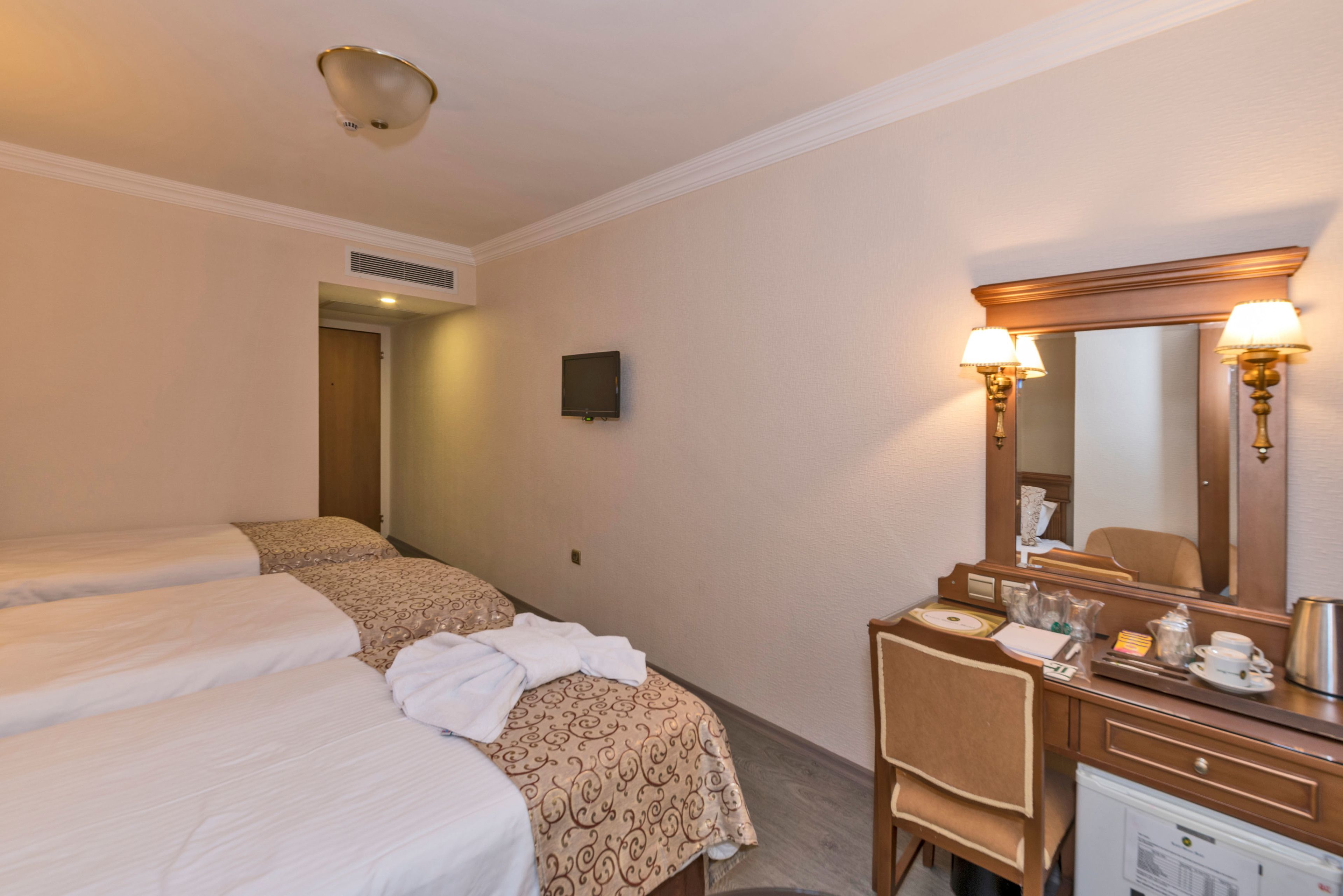 Una habitación de hotel con dos camas, un escritorio con espejo y una kitchenette pequeña.