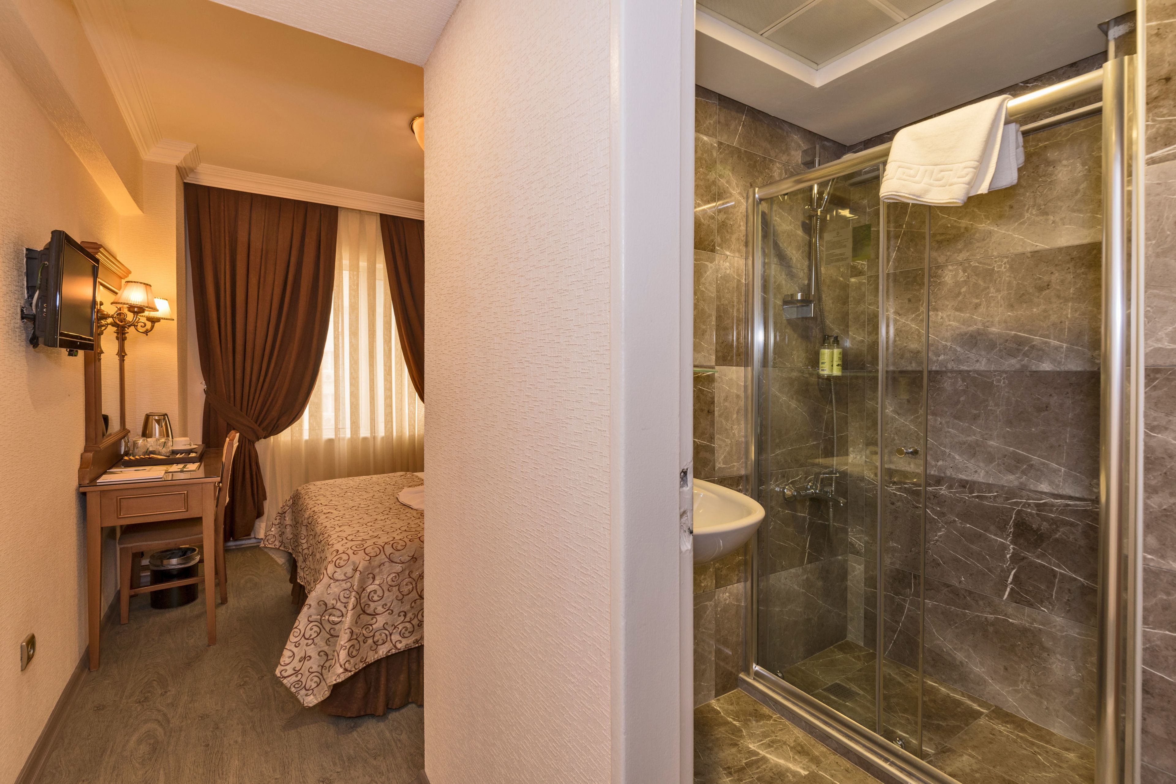 Hotelkamer met een bed, een bureau met lamp, douche met glazen deur en een badkamermeubel.
