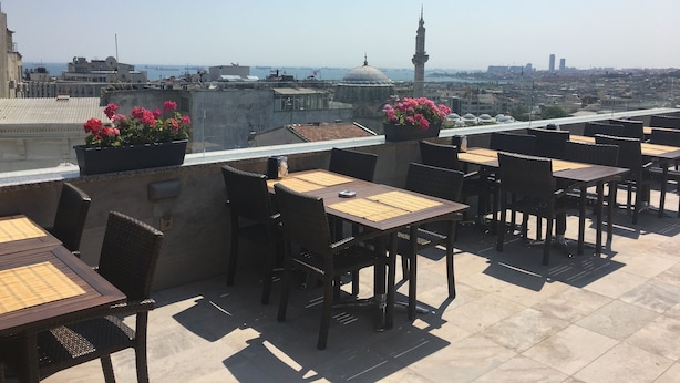Un espace extérieur aménagé avec des tables et des chaises, offrant une vue sur un paysage urbain composé d’immeubles et d’une mosquée.