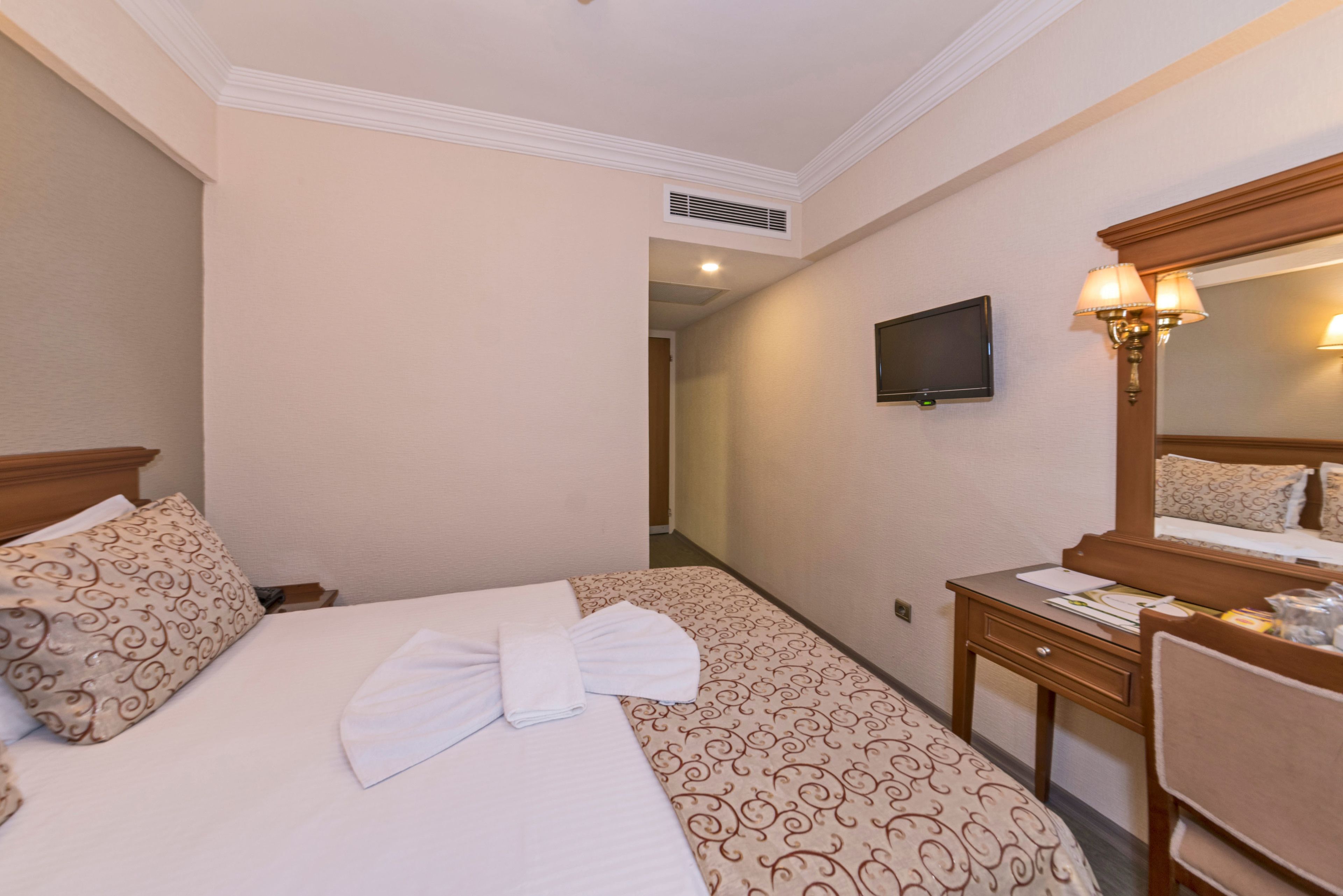 Une chambre d’hôtel équipée d’un lit, d’un bureau, d’une chaise, d’une télévision et d’un miroir.