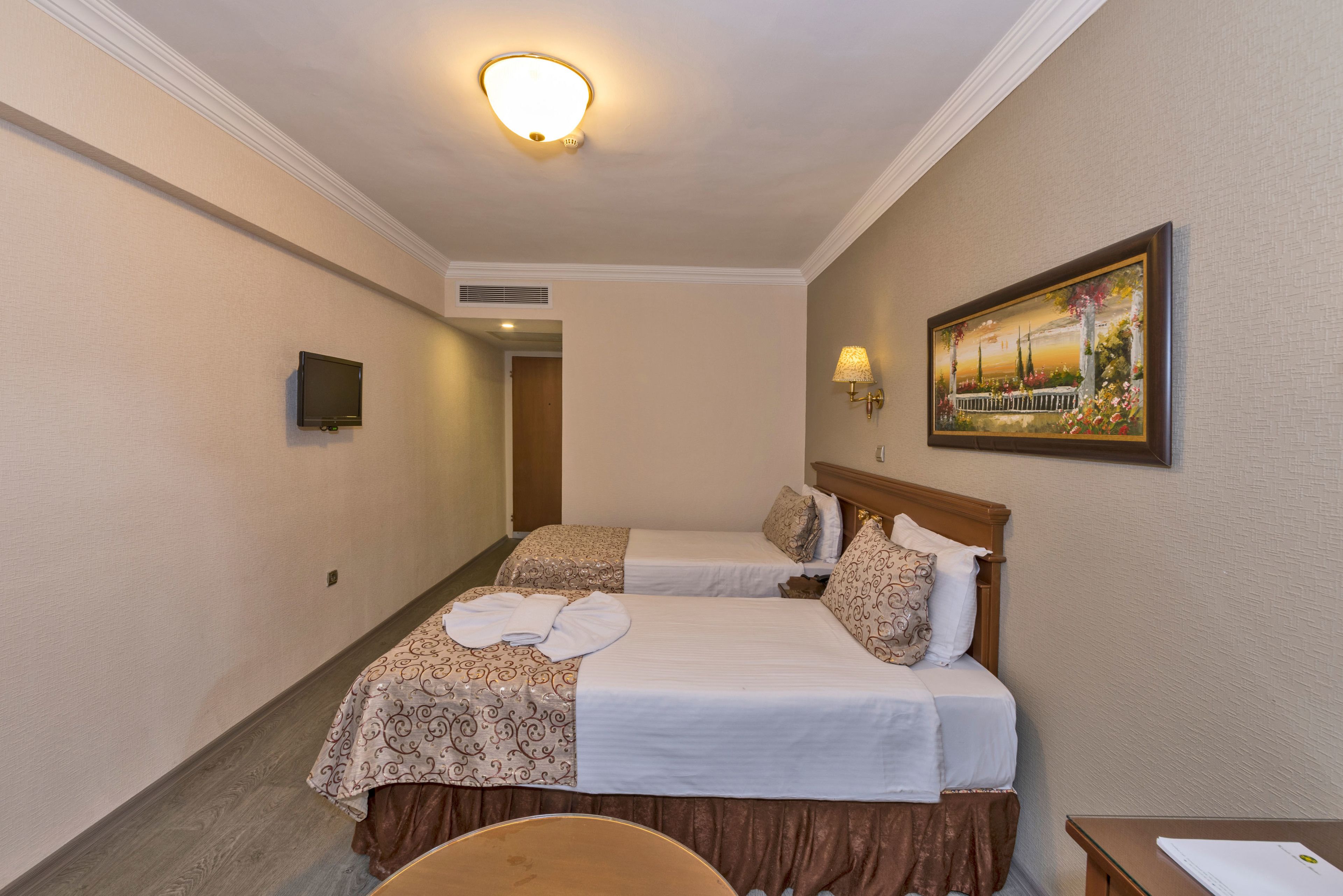 Camera d'albergo con due letti, una TV a schermo piatto, un quadro e una scrivania con una sedia.
