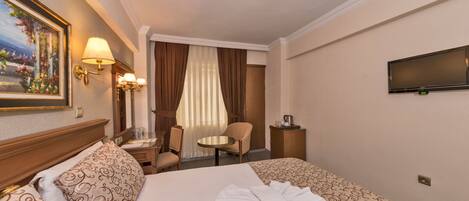 A hotel room with a large bed, a desk, a chair, a television, and a painting on the wall.