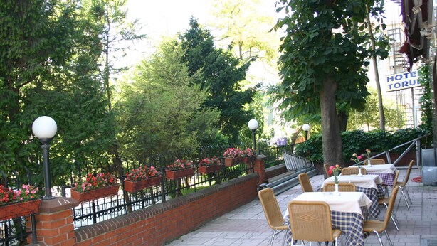 An outdoor cafe with tables and chairs, surrounded by a brick wall and greenery. - Yavuz Otel (Istanbul)