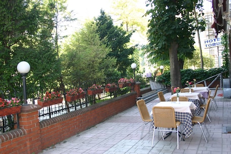 An outdoor cafe with tables and chairs, surrounded by a brick wall and greenery.