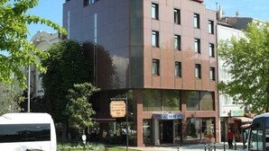 A modern building with a red roof and multiple windows. A bus is parked in front, and there is a sign for a hotel. - Yavuz Otel (Istanbul)