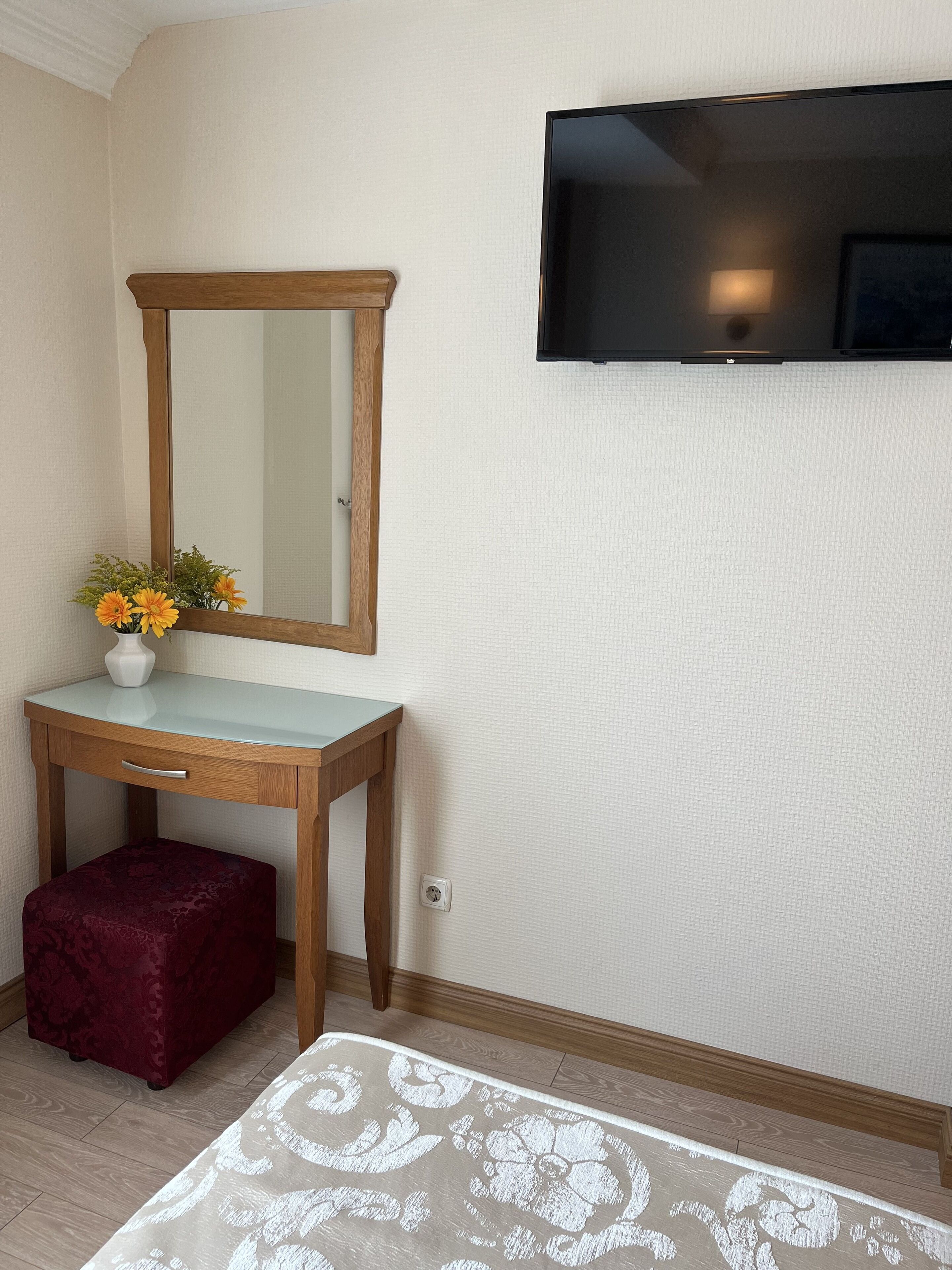 Una habitación pequeña con un tocador de madera, un espejo, un televisor fijado a la pared y una alfombra estampada en el suelo.