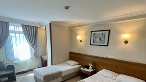 A hotel room with two single beds, a large bed, a desk with a chair, a radiator, and a window with curtains. - Yavuz Otel (Istanbul)