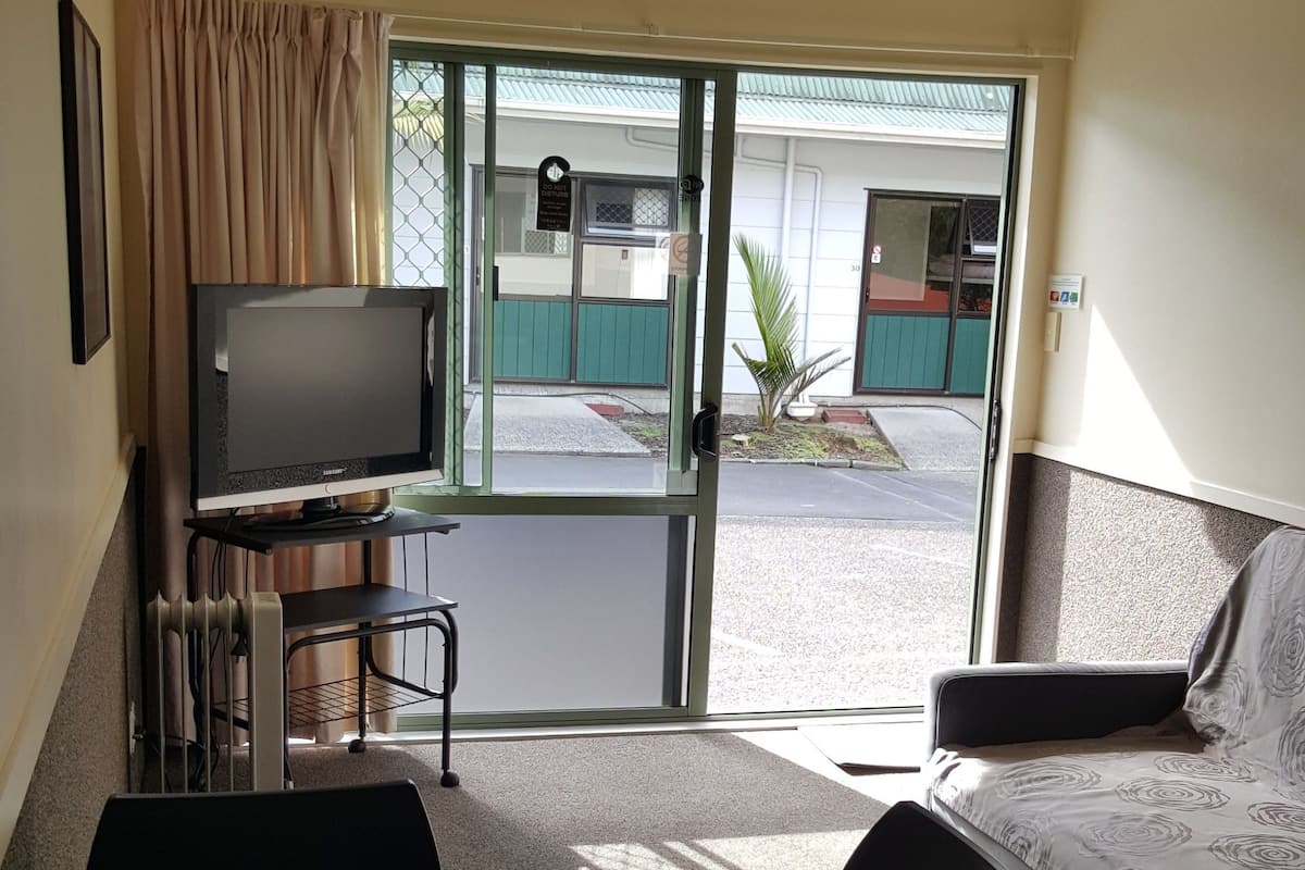Una habitación pequeña con una mesa redonda, cuatro sillas, un televisor y una ventana con cortinas.