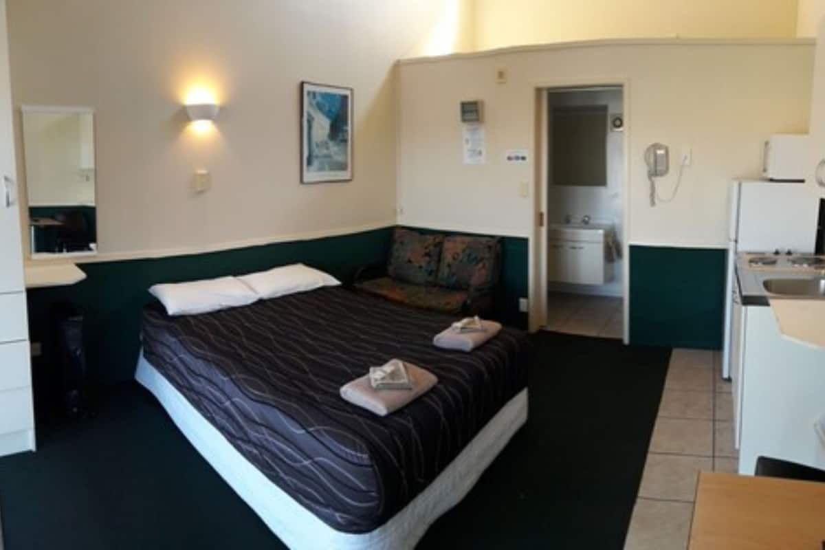 Habitación de hotel con cama, escritorio, espejo y kitchenette.