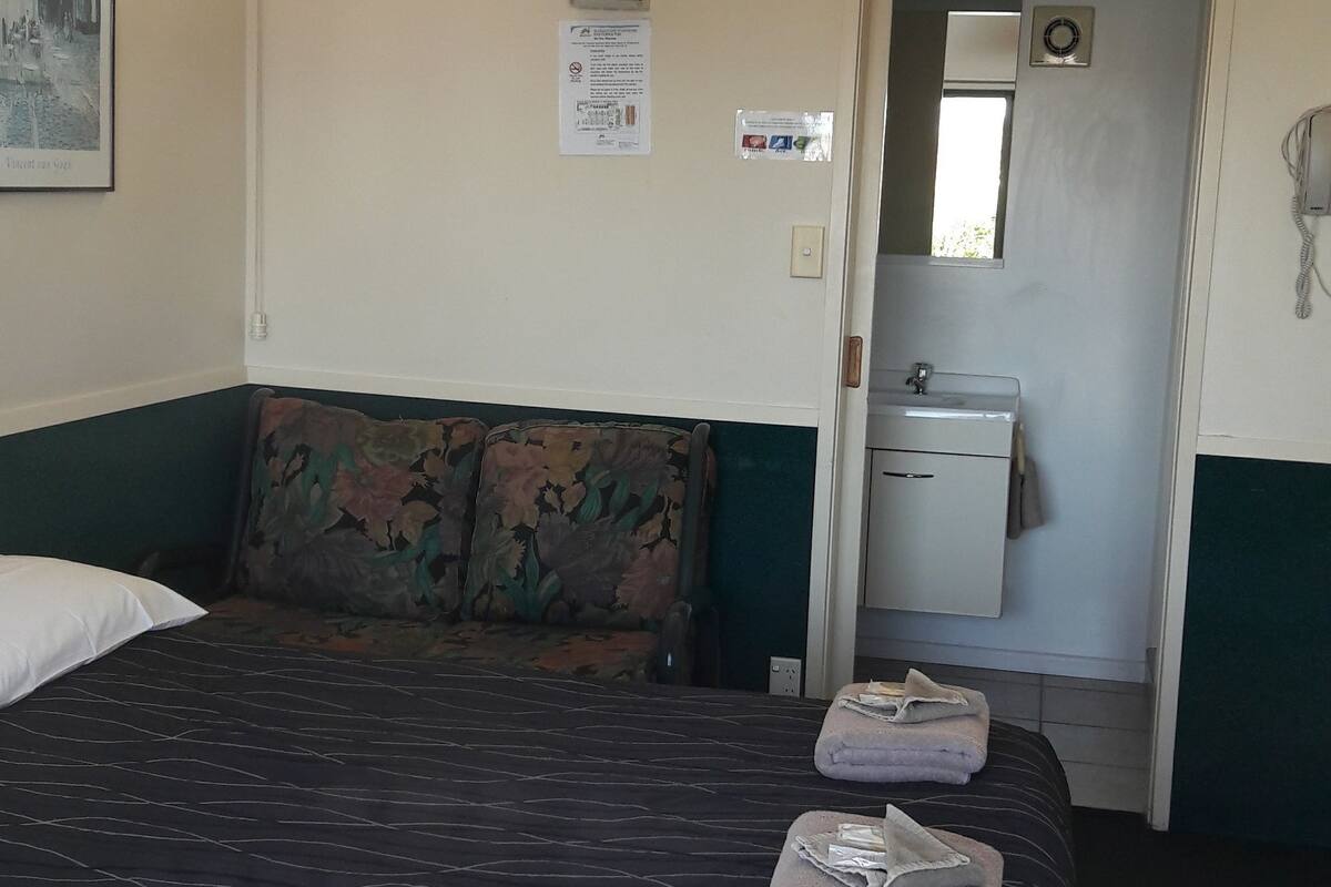 Habitación de hotel con cama, sofá, pequeña cocina y puerta de baño.