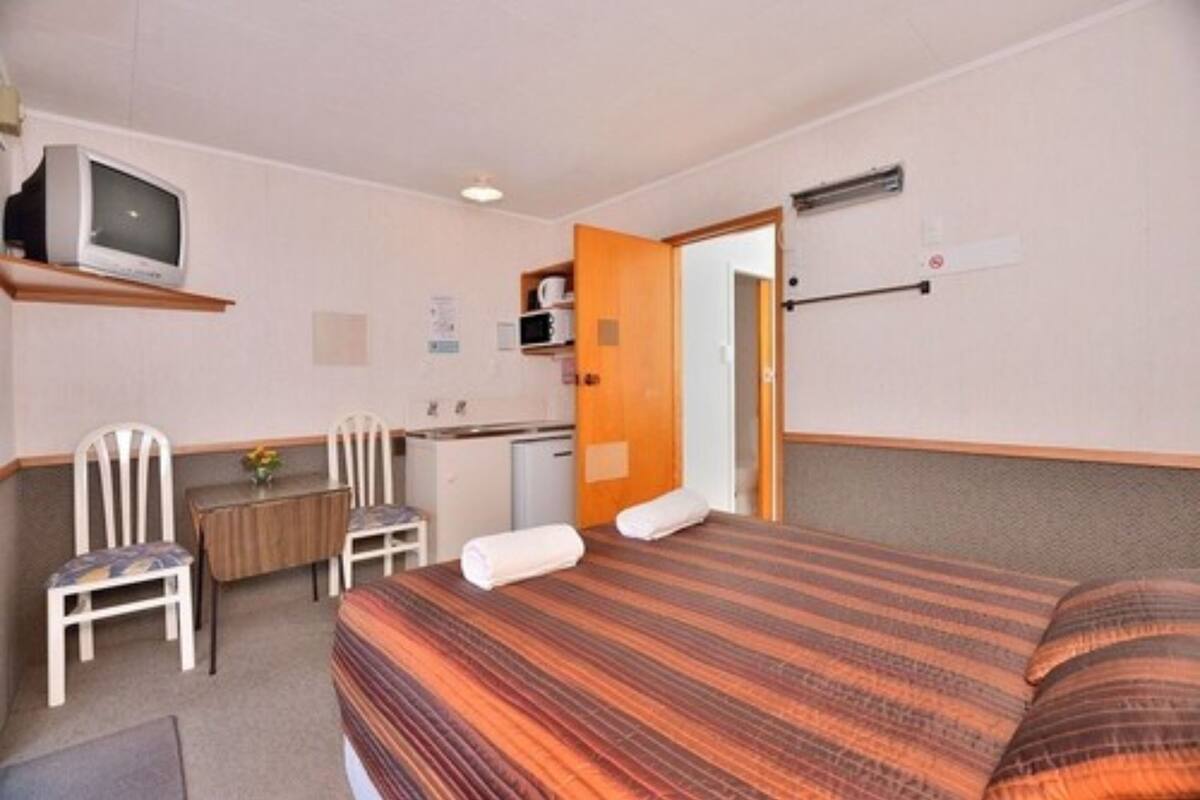 Una habitación de hotel con cama, escritorio, silla, televisión y microondas.
