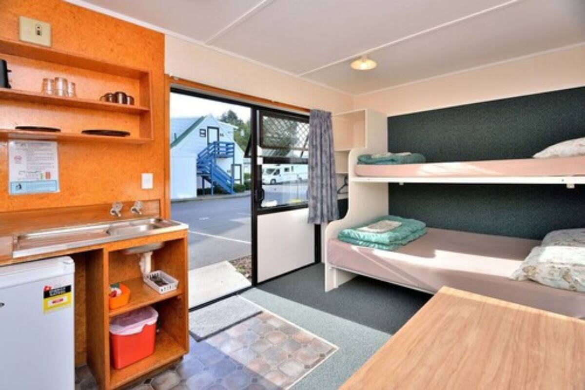 Habitación compacta con camas literas, una kitchenette pequeña y una ventana que ofrece vistas a un edificio.