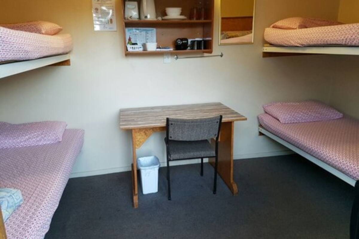 Un dormitorio con literas, un escritorio, una silla y un cubo de basura pequeño.