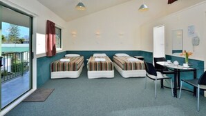 Ett hotellrum med tre enkelsängar, ett litet bord med stolar, ett fönster med gardiner och en dörr.