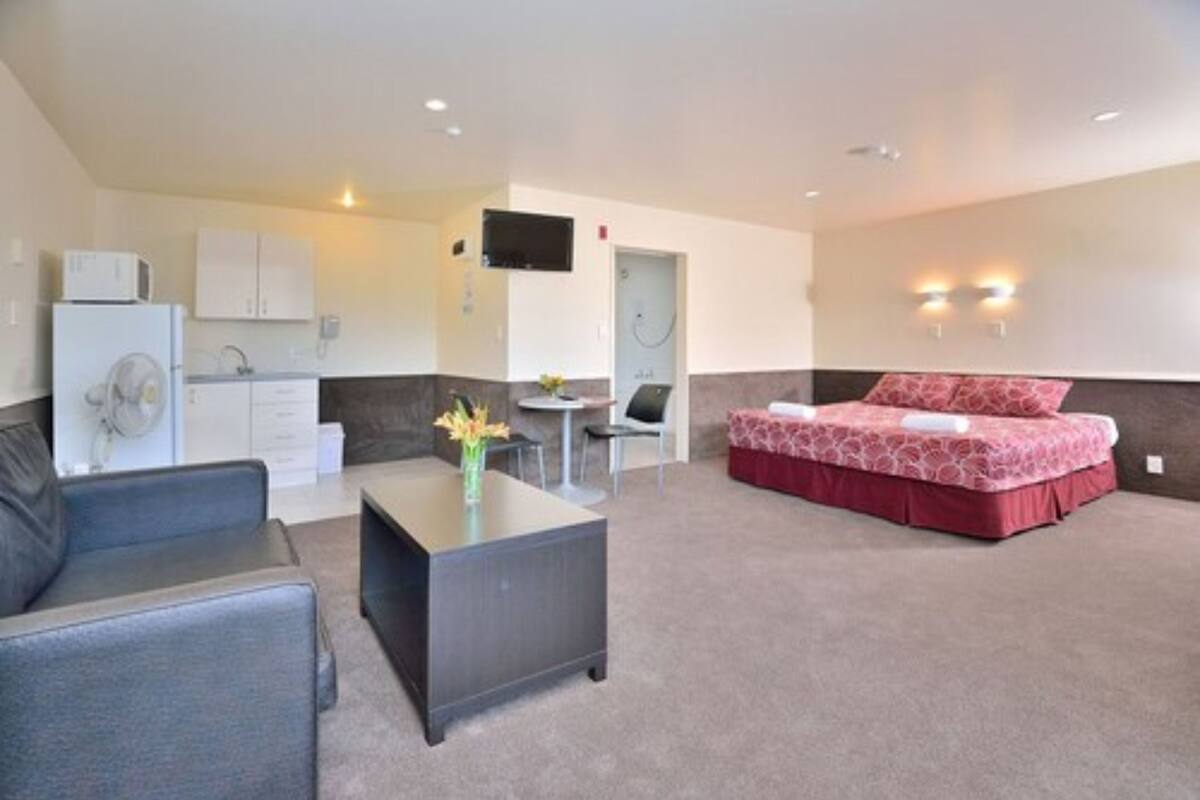 Habitación de hotel compacta con cama, kitchenette, zona de estar con mesa y sillas, y televisión montada en la pared.