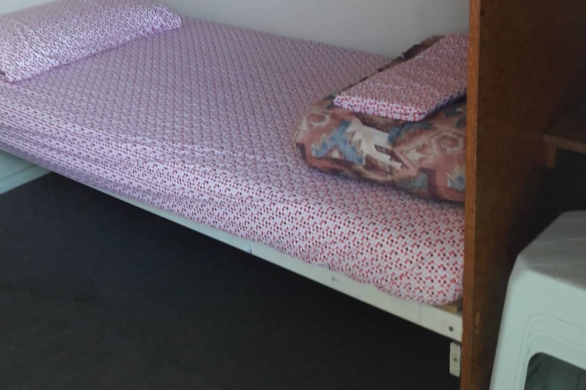 Una cama literera con ropa de cama estampada en una habitación con pared lisa y un objeto blanco pequeño a la derecha.