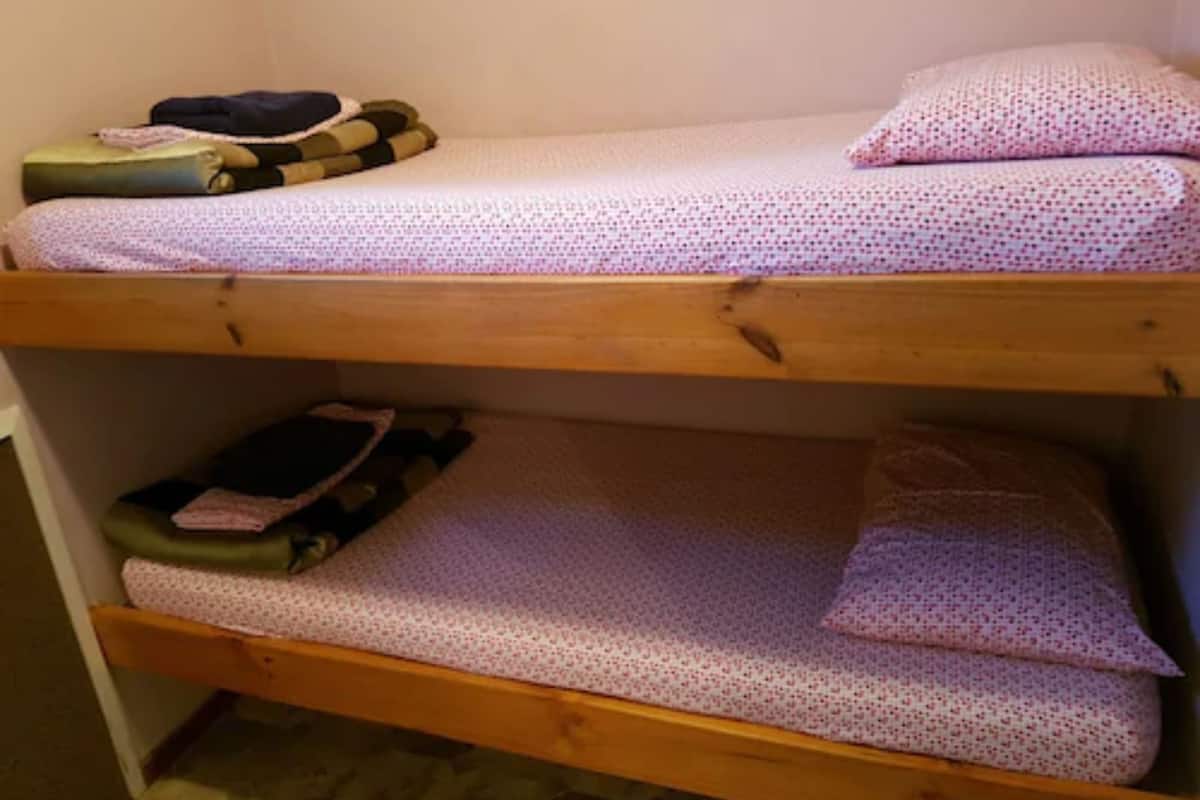 Una cama litera con colchón y almohadas estampadas, una chaqueta doblada y una mochila en la cama superior.