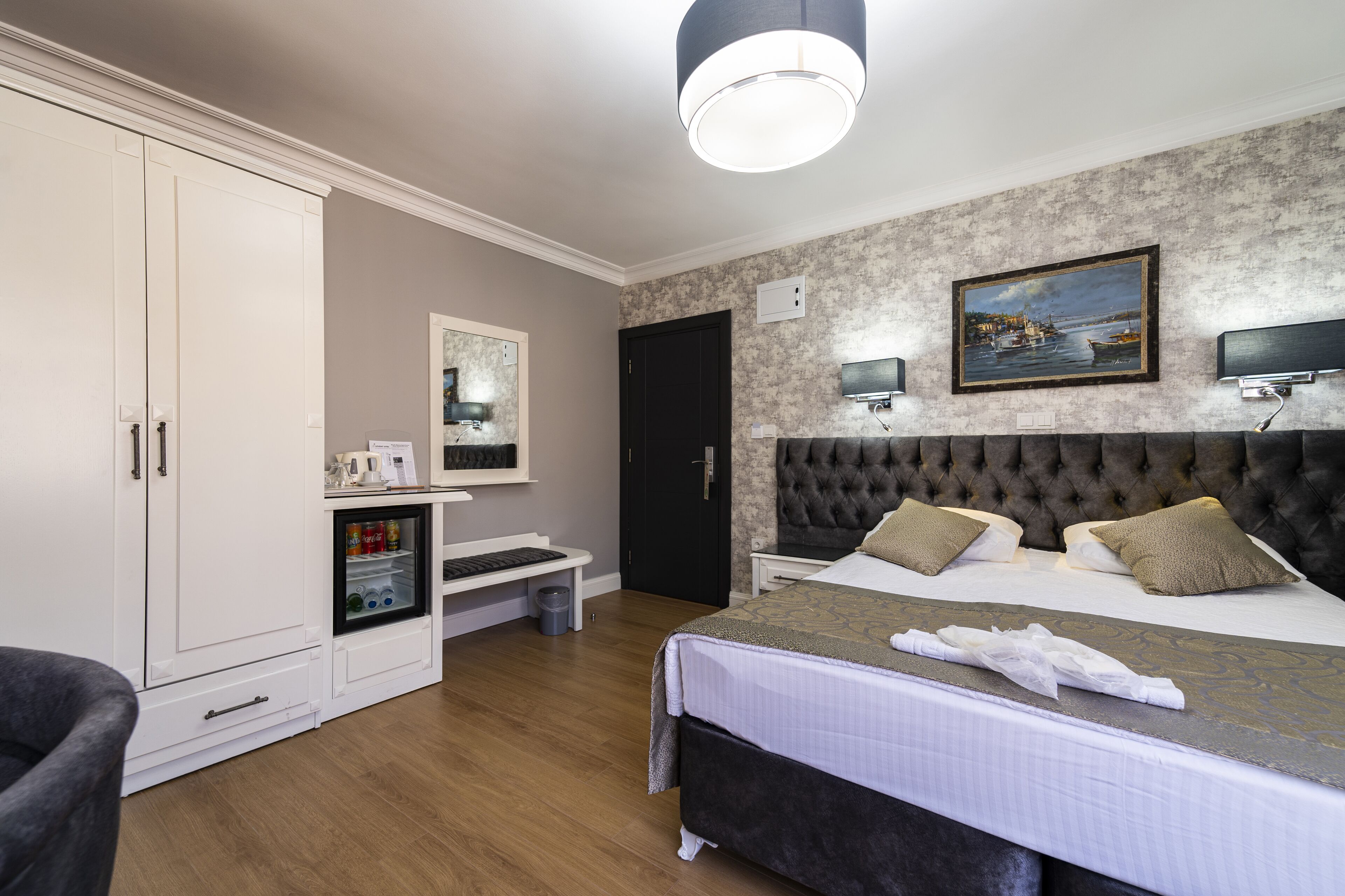 A hotel room with a large bed, a wardrobe, a desk with a computer, and a painting on the wall.