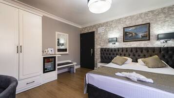 A hotel room with a large bed, a wardrobe, a desk with a computer, and a painting on the wall.