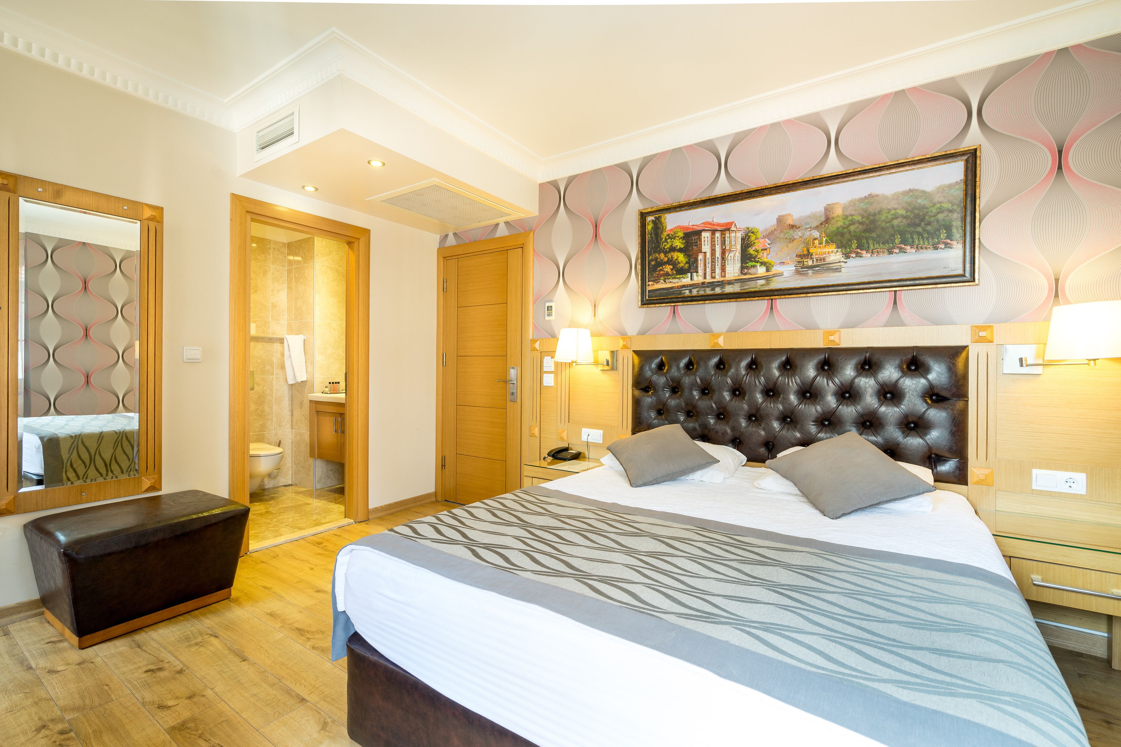 A hotel room with a large bed, a headboard, a bedside table, a mirror, and a bathroom visible through an open door.