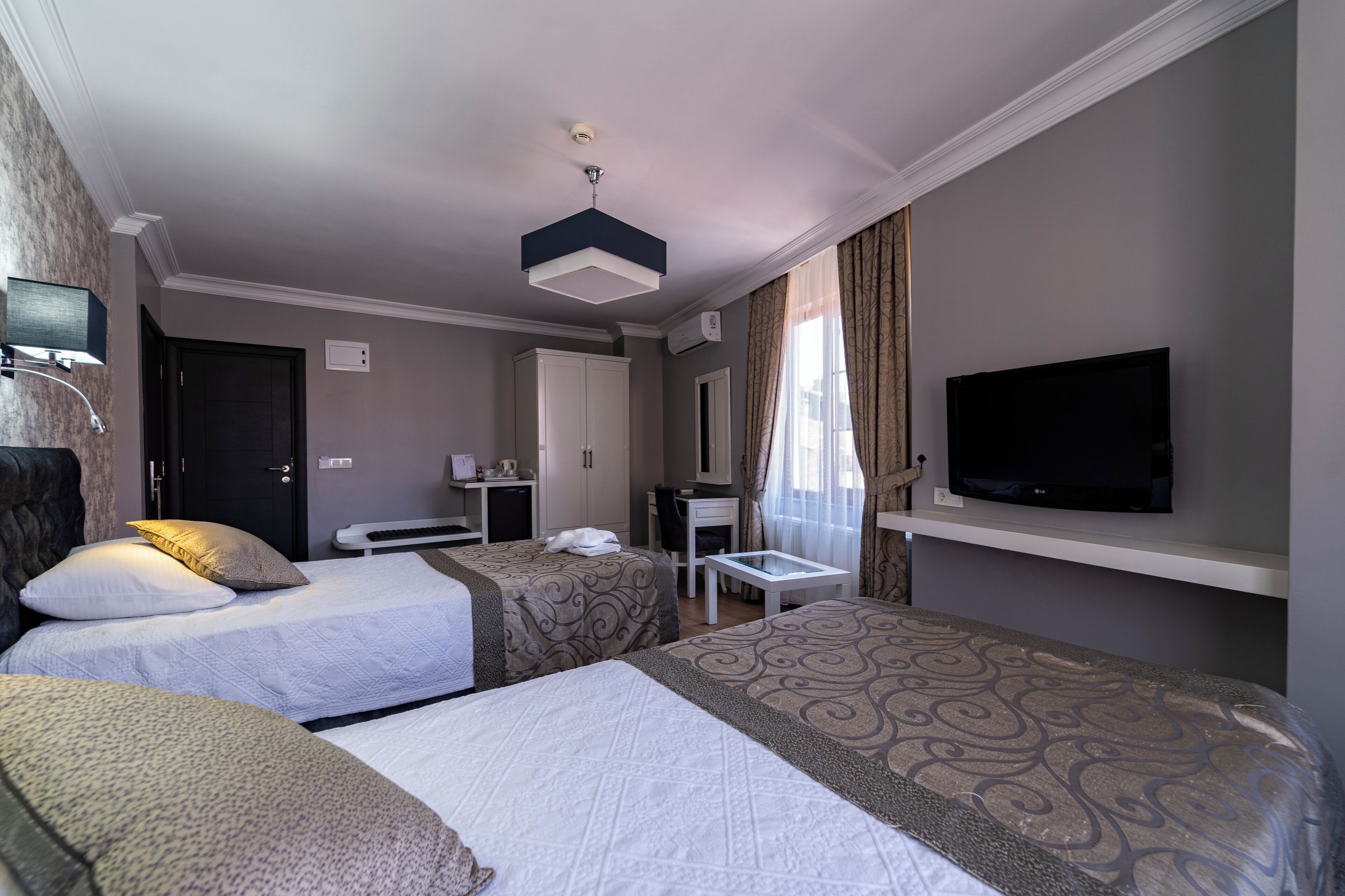A hotel room with two beds, a desk, a television, and an air conditioning unit.