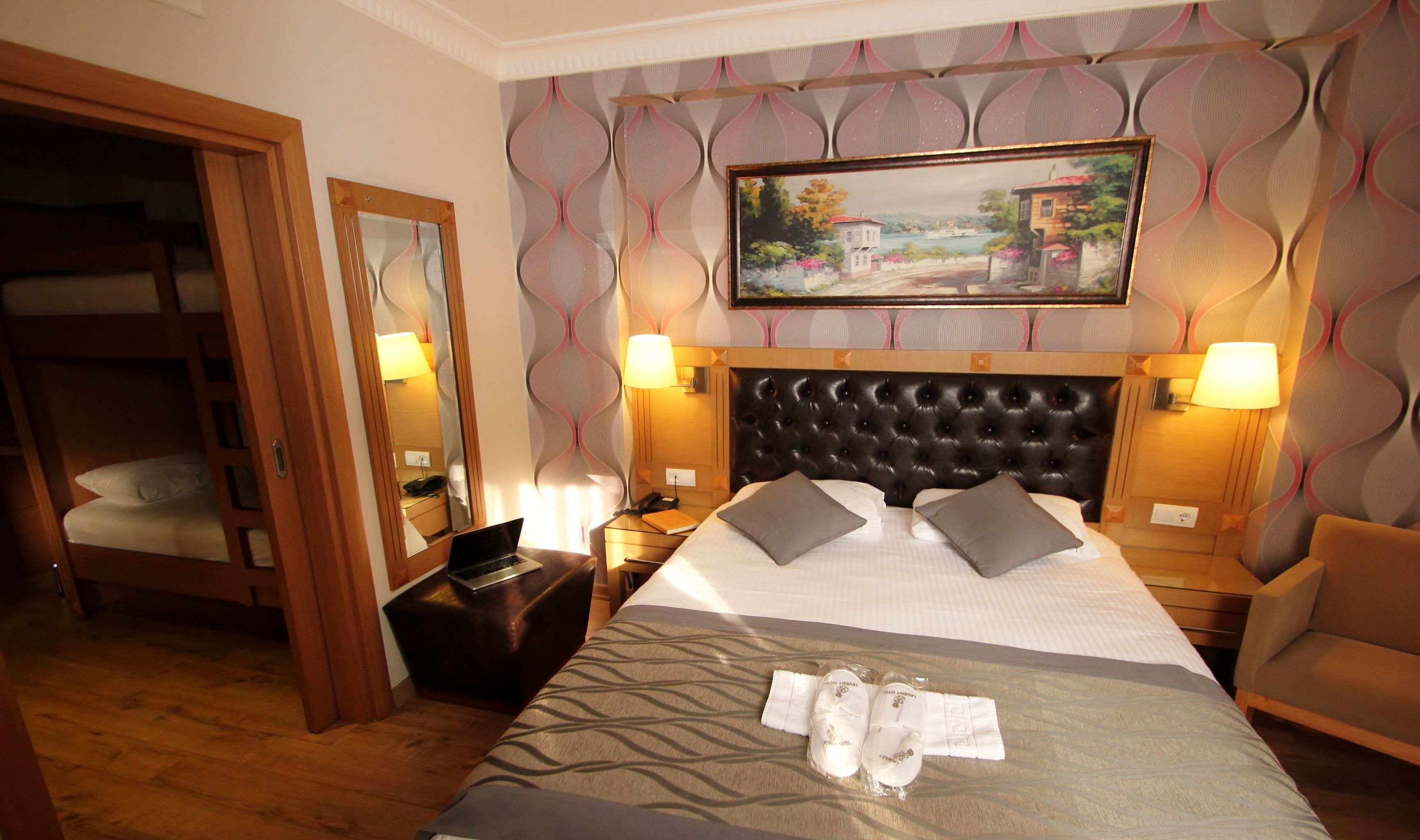 Hotelkamer met een groot bed, hoofdbord, twee bedlampen, een schilderij aan de muur, een houten garderobe en een spiegel.