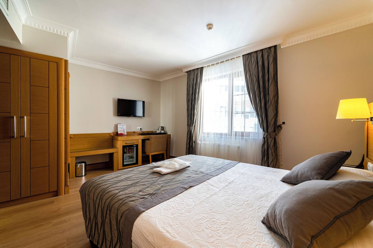 Una habitación de hotel con una cama grande, un escritorio, un televisor y una ventana con cortinas.