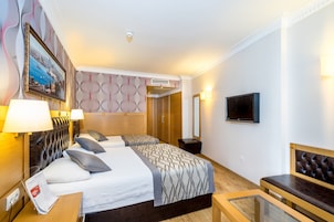 Habitación de hotel con dos camas, televisión, un banco y un cuadro en la pared.
